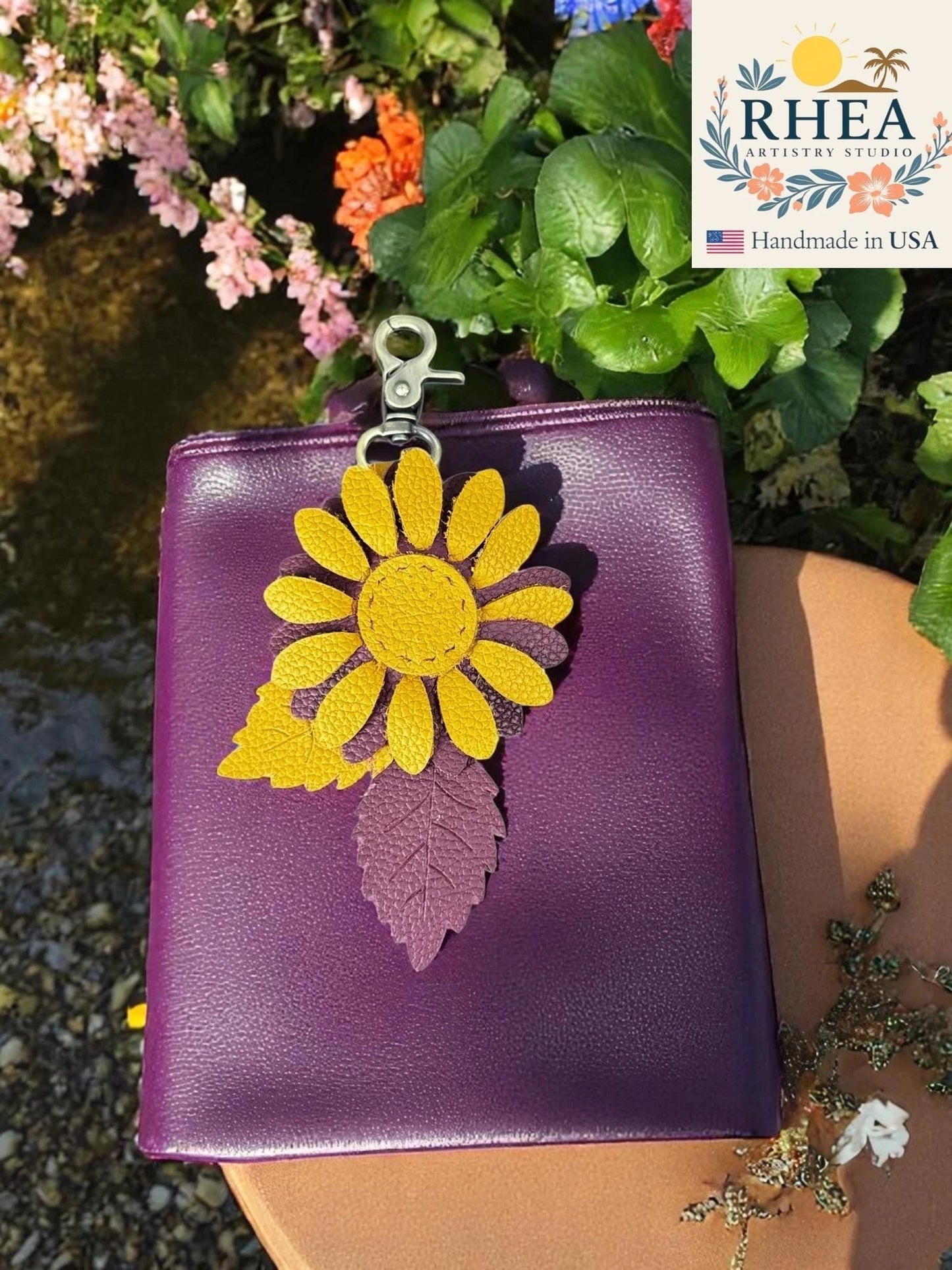 Rhea Artistry Studio purple leather bag with a yellow and purple leather daisy charm featuring a textured leaf detail and brass hardware.