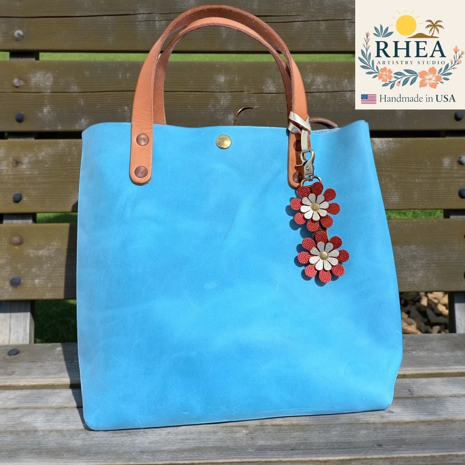 Rhea Artistry Studio handmade double-layer leather daisy purse charm in red and gold, attached to a blue tote bag.