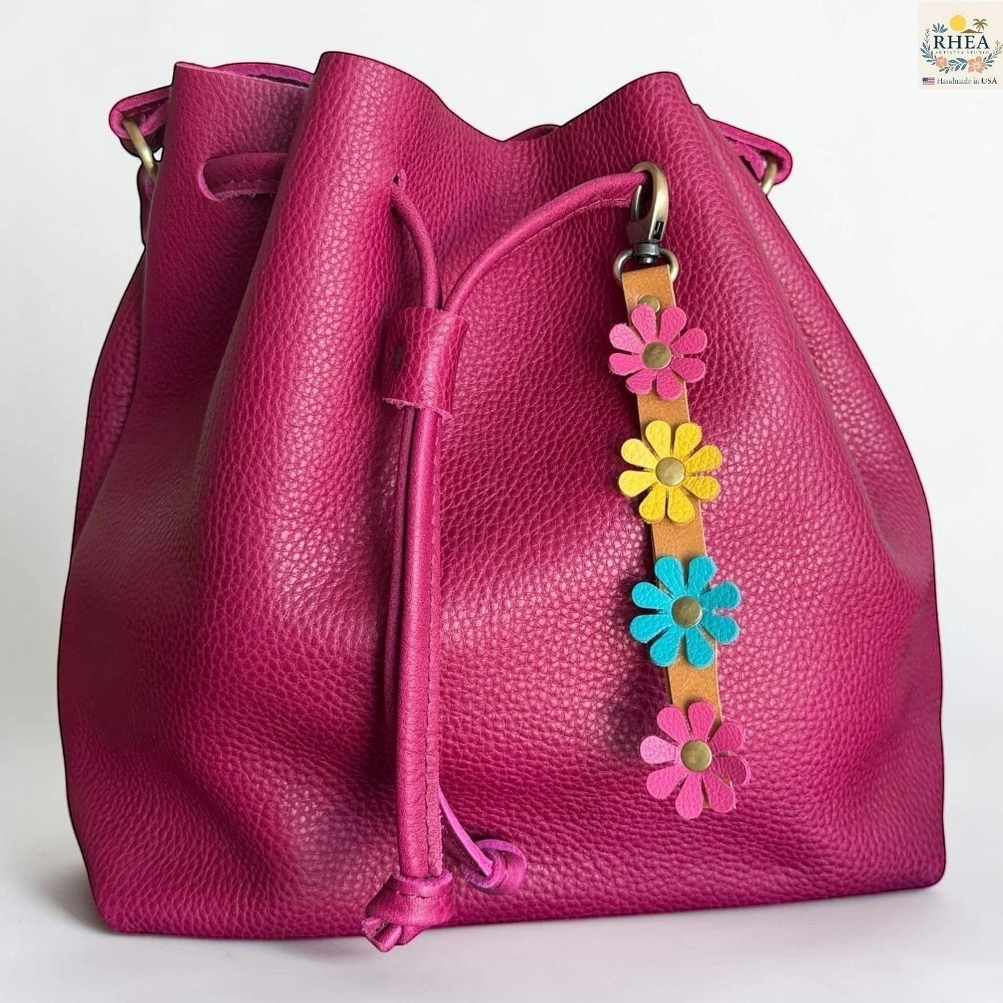 Rhea Artistry Studio handmade leather daisy wristlet keychain with pink, yellow, and blue flowers attached to a tan leather strap with brass rivets.