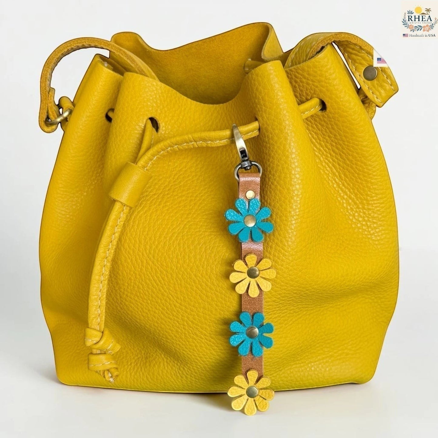Rhea Artistry Studio handmade leather daisy wristlet keychain with blue and yellow flowers attached to a yellow bucket bag.