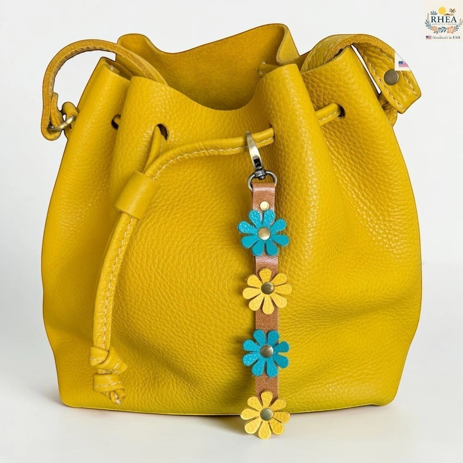 Rhea Artistry Studio handmade leather daisy wristlet keychain with blue and yellow flowers attached to a yellow bucket bag.