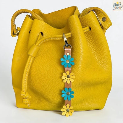 Rhea Artistry Studio handmade leather daisy wristlet keychain with yellow and blue flowers on a brown strap, attached to a yellow bucket bag.