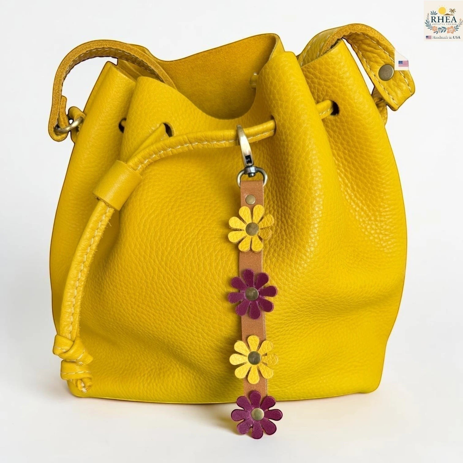 Rhea Artistry Studio handmade leather daisy wristlet keychain with yellow and purple flowers attached to a yellow bucket bag.