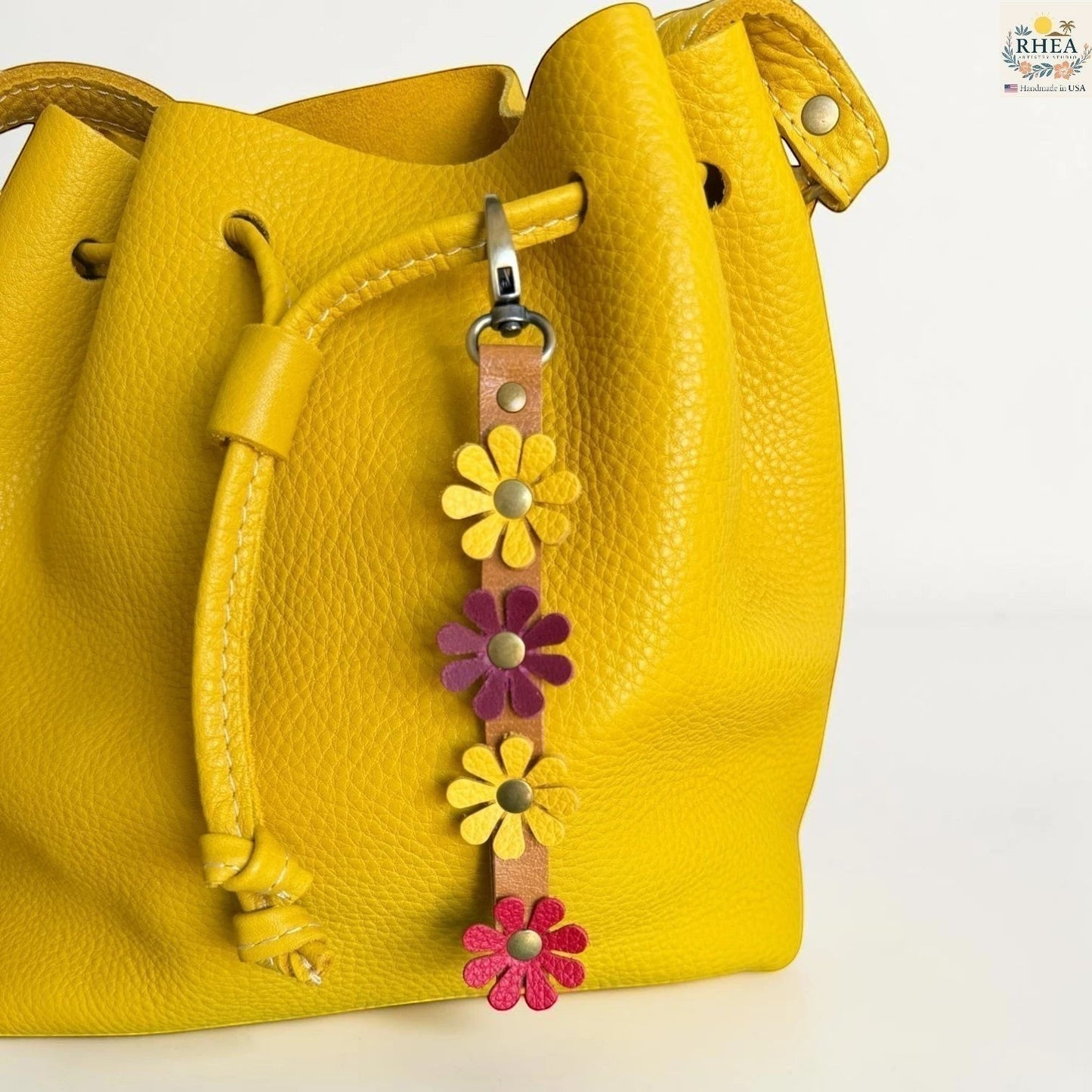 Rhea Artistry Studio handmade leather daisy wristlet keychain with yellow, pink, and purple flowers attached to a tan leather strap with brass rivets.