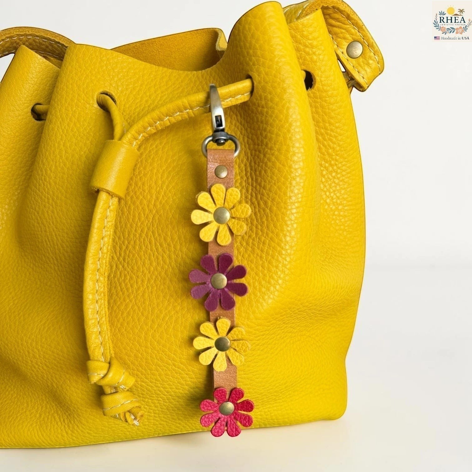 Rhea Artistry Studio handmade leather daisy wristlet keychain with yellow, pink, and purple flowers attached to a tan leather strap with brass rivets.