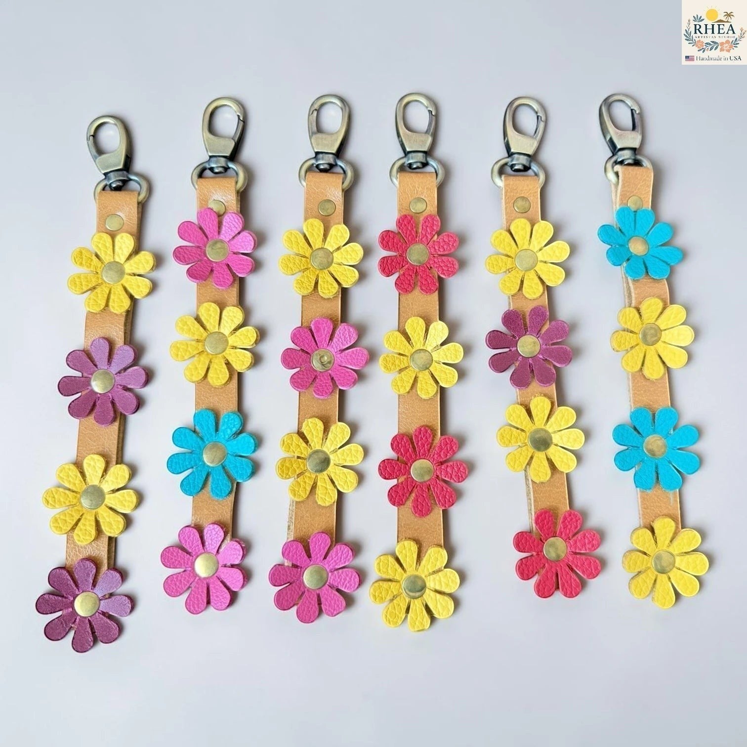 Rhea Artistry Studio handmade leather daisy wristlet keychains in yellow, pink, purple, and blue with brass hardware.
