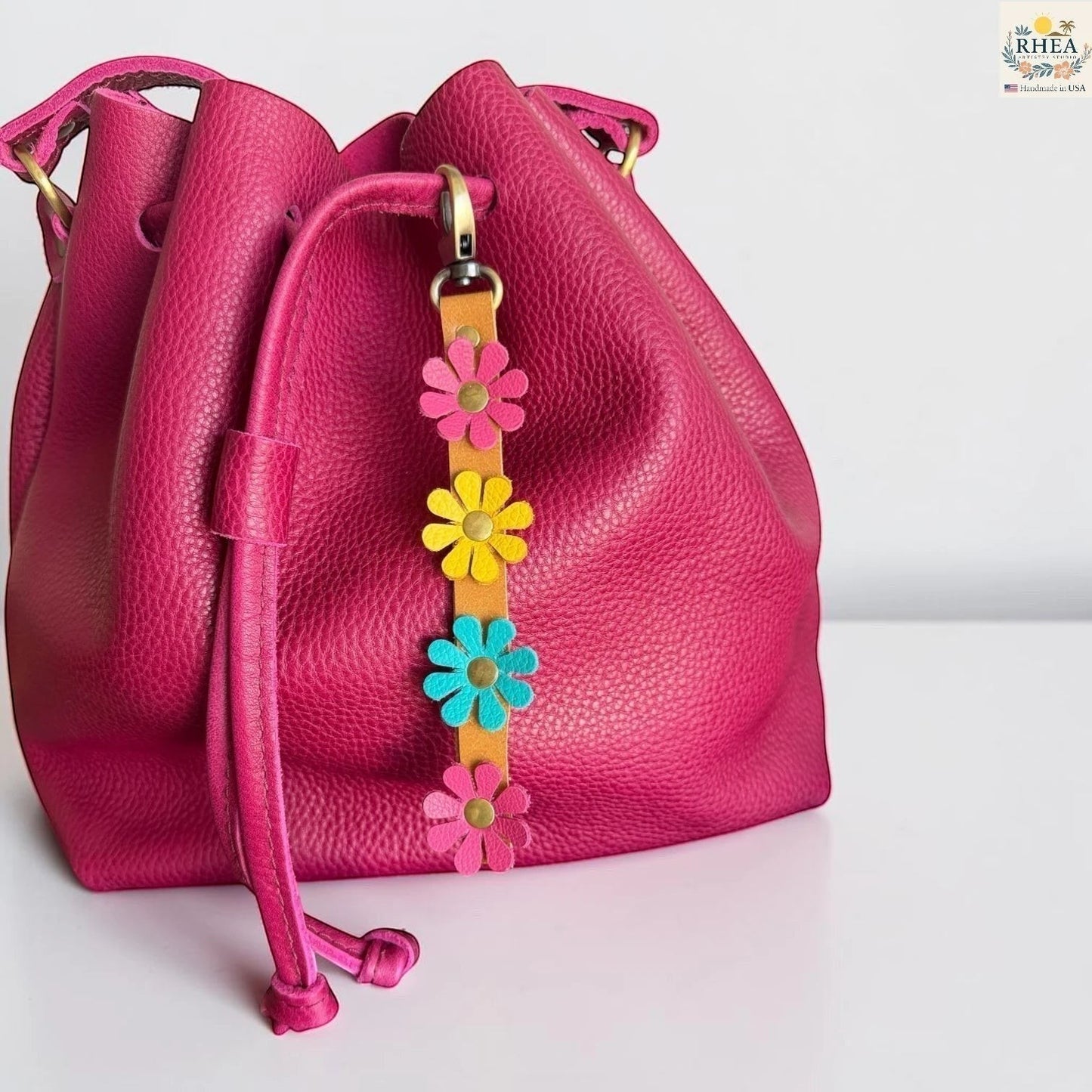 Rhea Artistry Studio handmade leather daisy wristlet keychain with pink, yellow, and teal flowers attached to a tan leather strap with brass rivets.