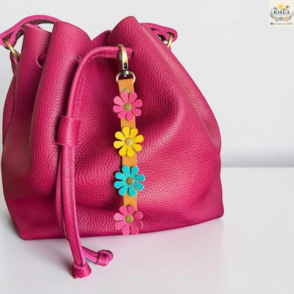 Rhea Artistry Studio handmade leather daisy wristlet keychain with pink, yellow, and teal flowers attached to a tan leather strap with brass rivets.