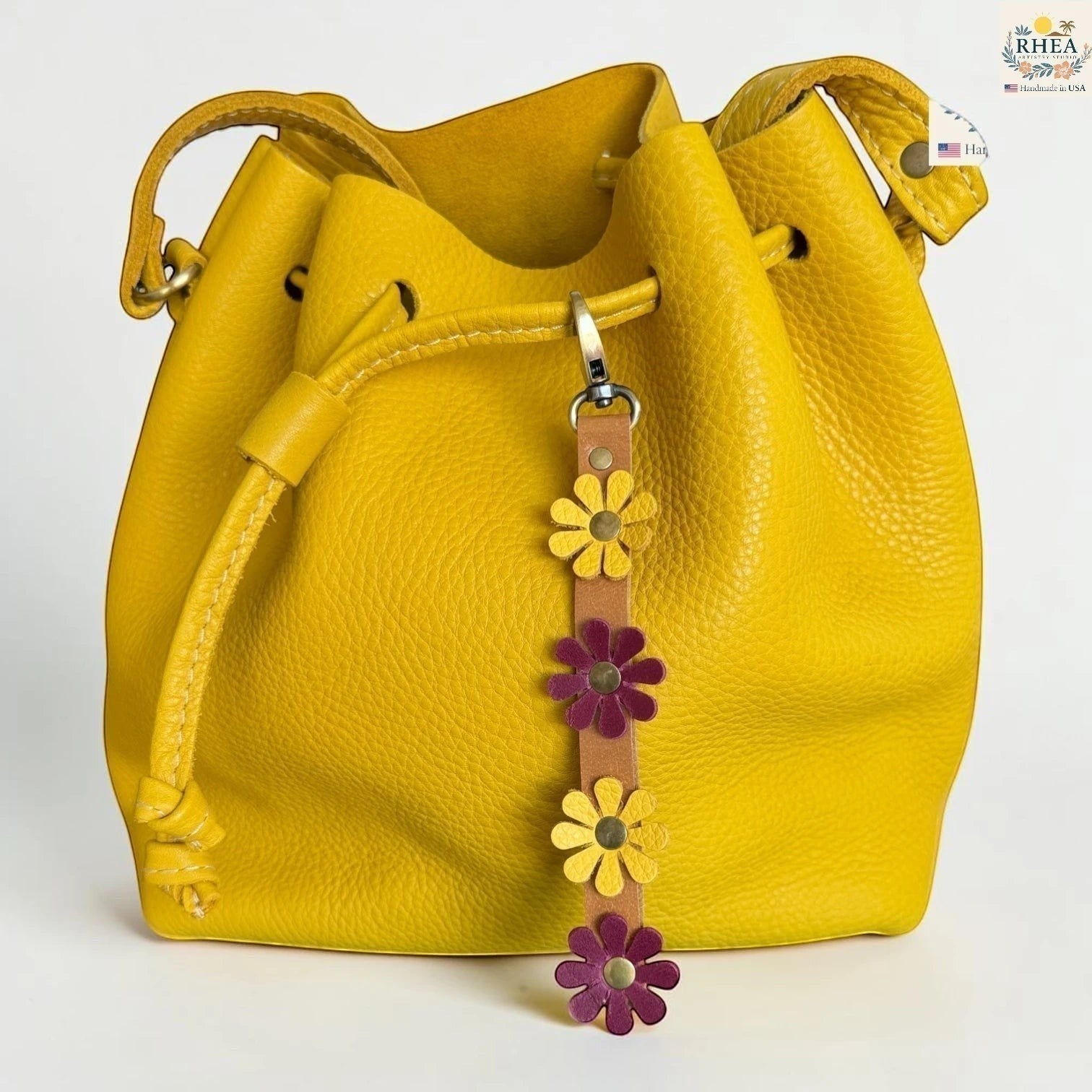 Rhea Artistry Studio yellow leather daisy wristlet keychain with purple and yellow flowers and brass rivets, attached to a yellow bucket bag.