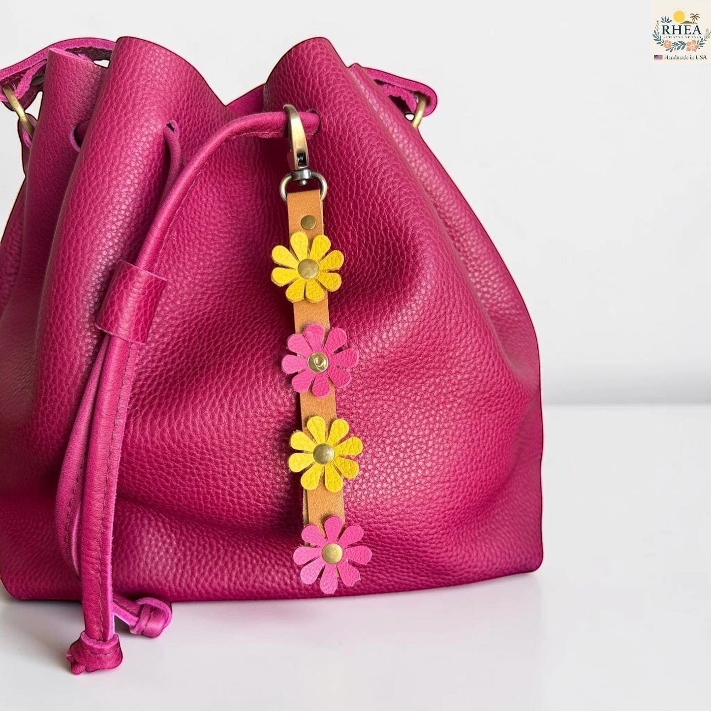Rhea Artistry Studio handmade leather daisy wristlet keychain with pink and yellow flowers attached to a tan leather strap with brass rivets.