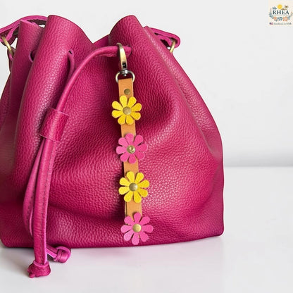 Rhea Artistry Studio handmade leather daisy wristlet keychain with pink and yellow flowers attached to a tan leather strap with brass rivets.