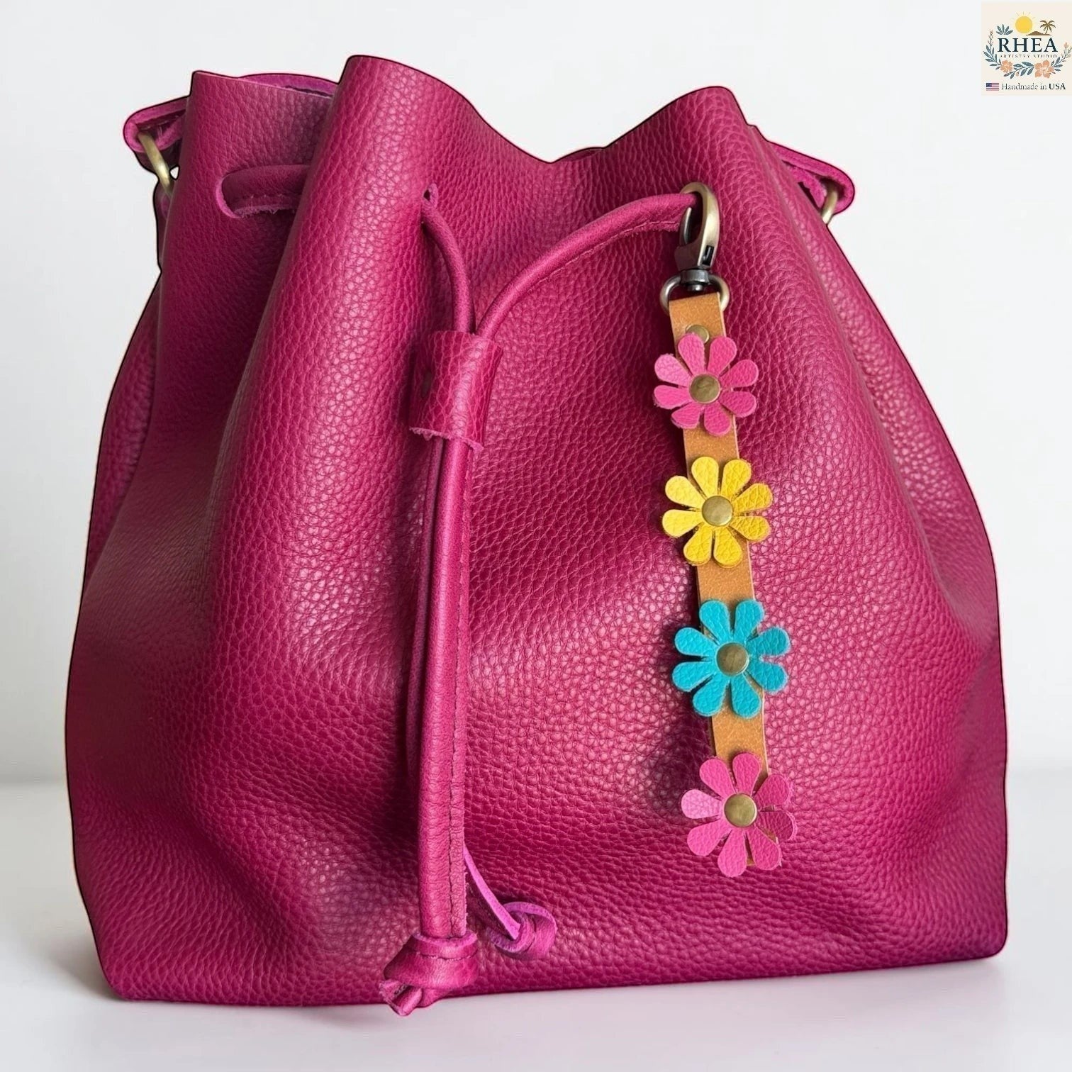 Rhea Artistry Studio handmade leather daisy wristlet keychain with pink, yellow, and blue flowers attached to a tan leather strap with brass rivets.