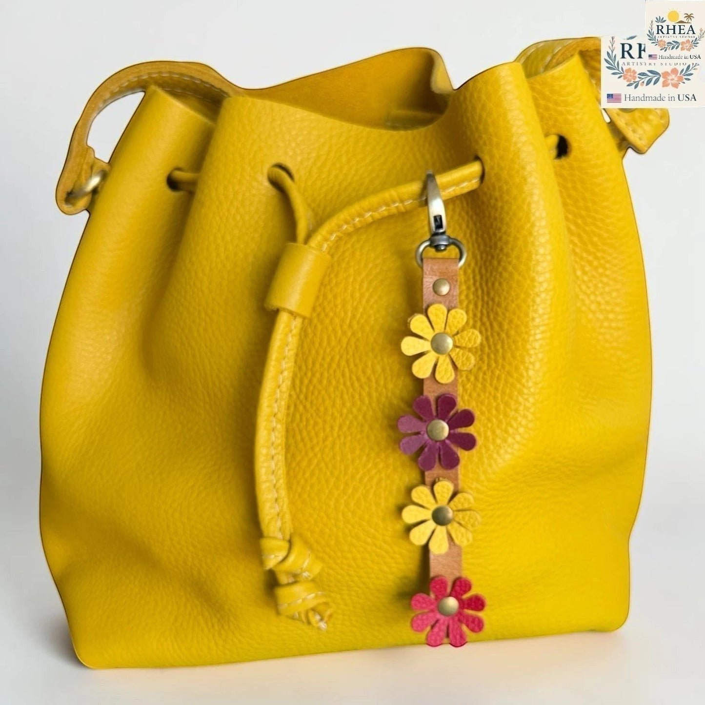 Rhea Artistry Studio handmade leather daisy wristlet keychain with yellow, pink, and purple flowers attached to a yellow bucket bag.