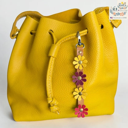 Rhea Artistry Studio handmade leather daisy wristlet keychain with yellow, pink, and purple flowers attached to a yellow bucket bag.