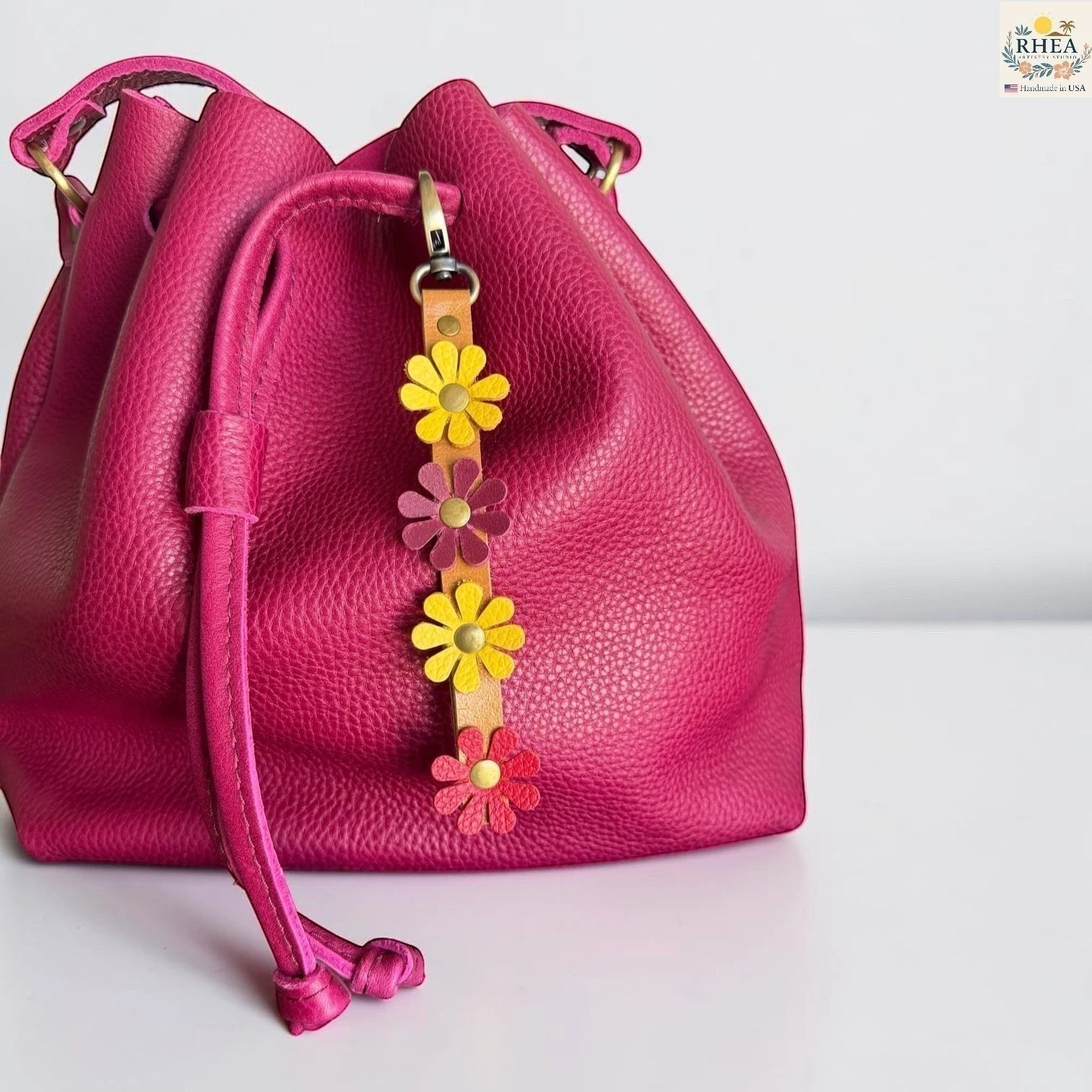 Rhea Artistry Studio handmade leather daisy wristlet keychain with yellow, burgundy, and red flowers attached to a tan strap with brass rivets.