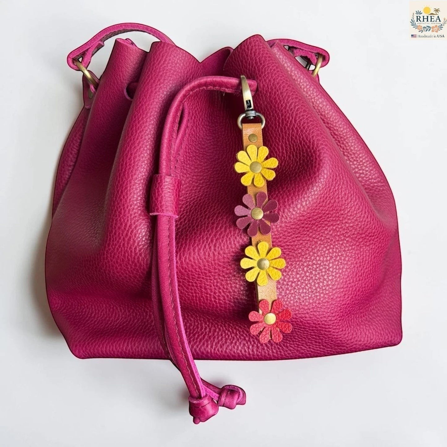 Rhea Artistry Studio handmade leather daisy wristlet keychain with yellow, purple, and pink flowers attached to a tan leather strap with brass rivets.
