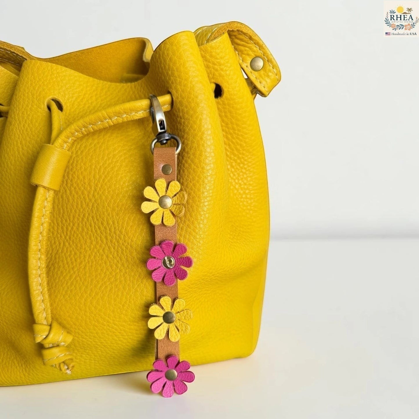 Rhea Artistry Studio handmade leather daisy wristlet keychain with yellow and pink flowers attached to a yellow bucket bag.