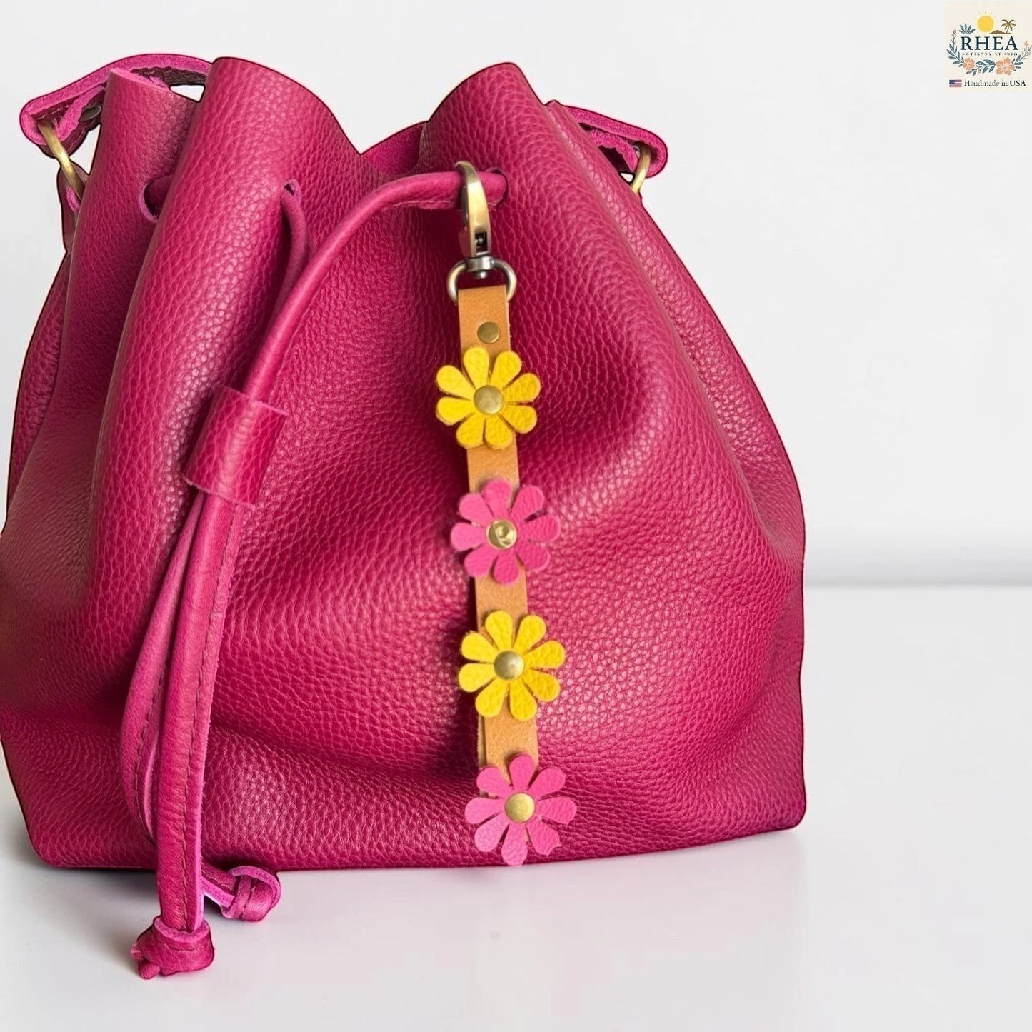 Rhea Artistry Studio handmade leather daisy wristlet keychain in pink and yellow with brass hardware on a fuchsia bucket bag.