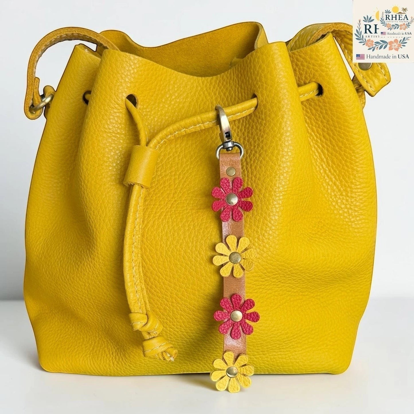 Rhea Artistry Studio handmade leather daisy wristlet keychain with pink and yellow flowers attached to a tan leather strap with brass rivets.