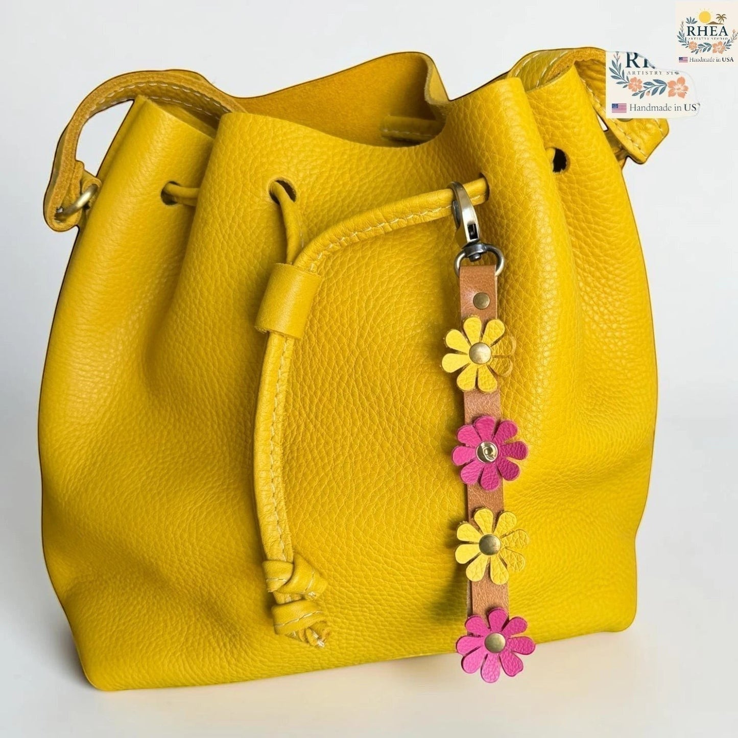 Rhea Artistry Studio yellow leather daisy wristlet keychain with pink and yellow flowers and brass rivets attached to a yellow bucket bag.