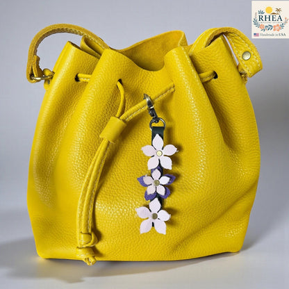 Rhea Artistry Studio yellow leather bucket bag with a handmade leather floral charm featuring light pink and purple flowers and a brushed brass clasp.