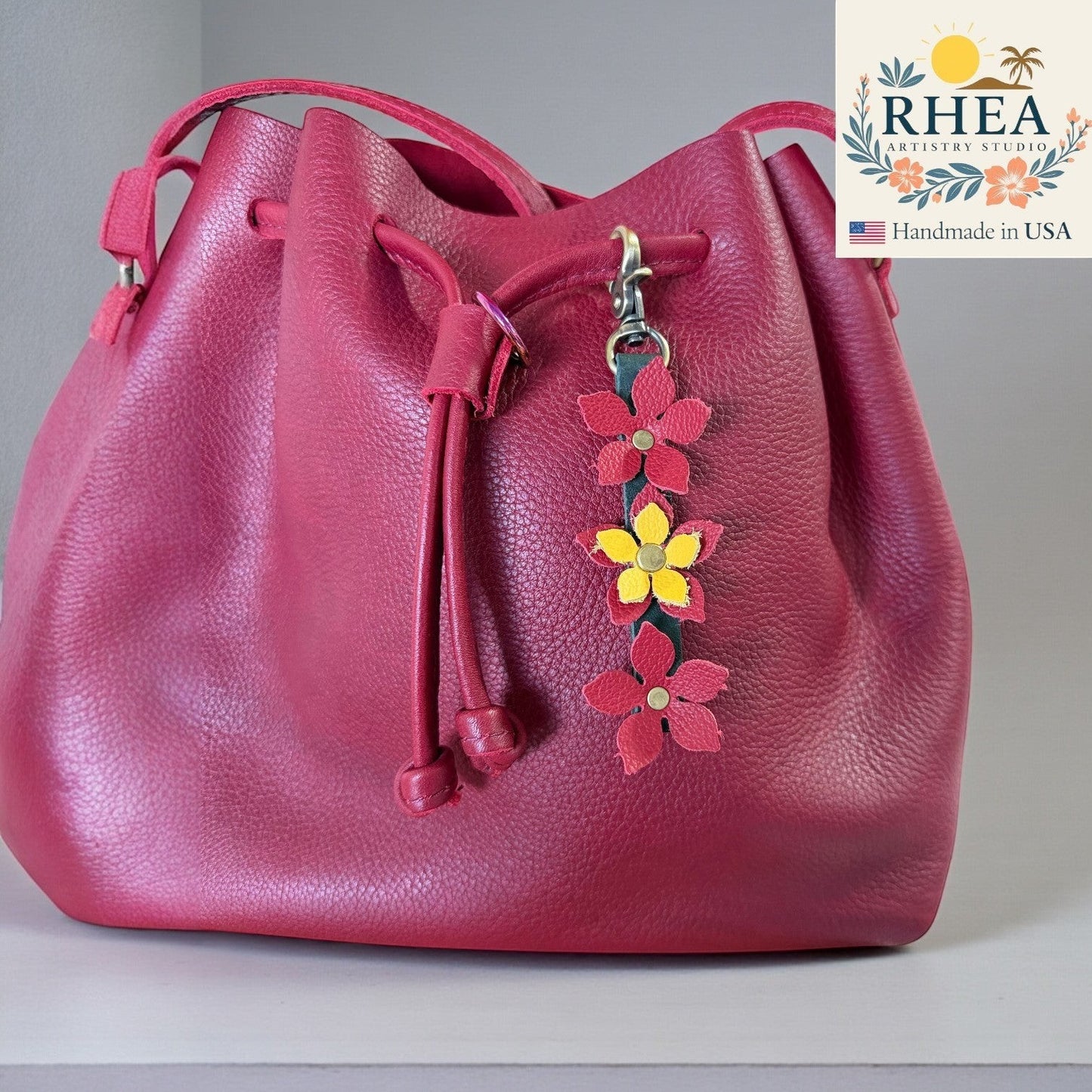 Rhea Artistry Studio handmade leather floral charm with red and yellow flowers and a brushed brass clasp attached to a magenta bucket bag.