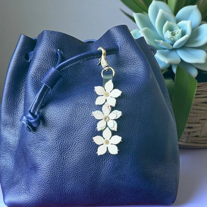 Rhea Artistry Studio navy blue leather drawstring bag with a handmade floral charm featuring white leather flowers and a brushed brass clasp.