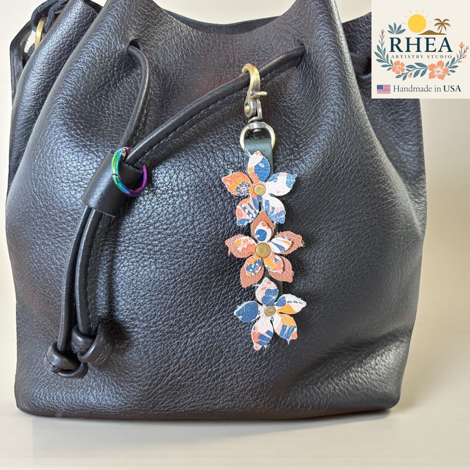 Rhea Artistry Studio handmade leather floral charm with brushed brass clasp, featuring blue and coral flowers.