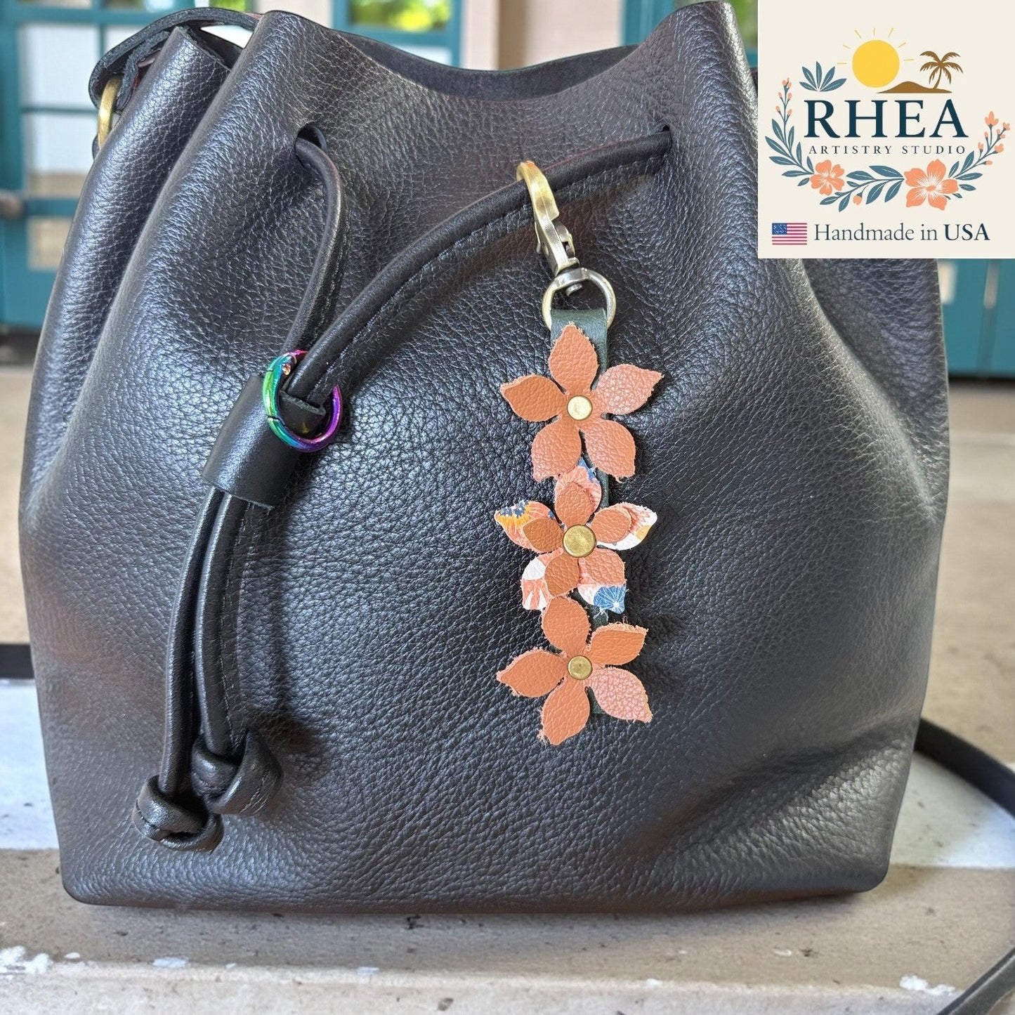 Rhea Artistry Studio handmade leather floral charm with brushed brass clasp, featuring three orange leather flowers with patterned centers.