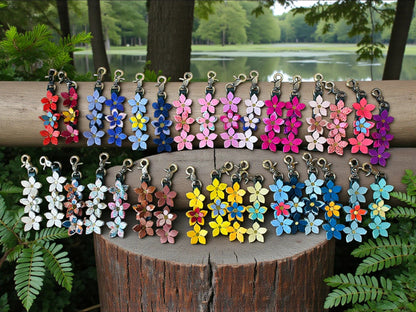 Rhea Artistry Studio handmade leather floral charms in various colors with brushed brass clasps, displayed on wood.