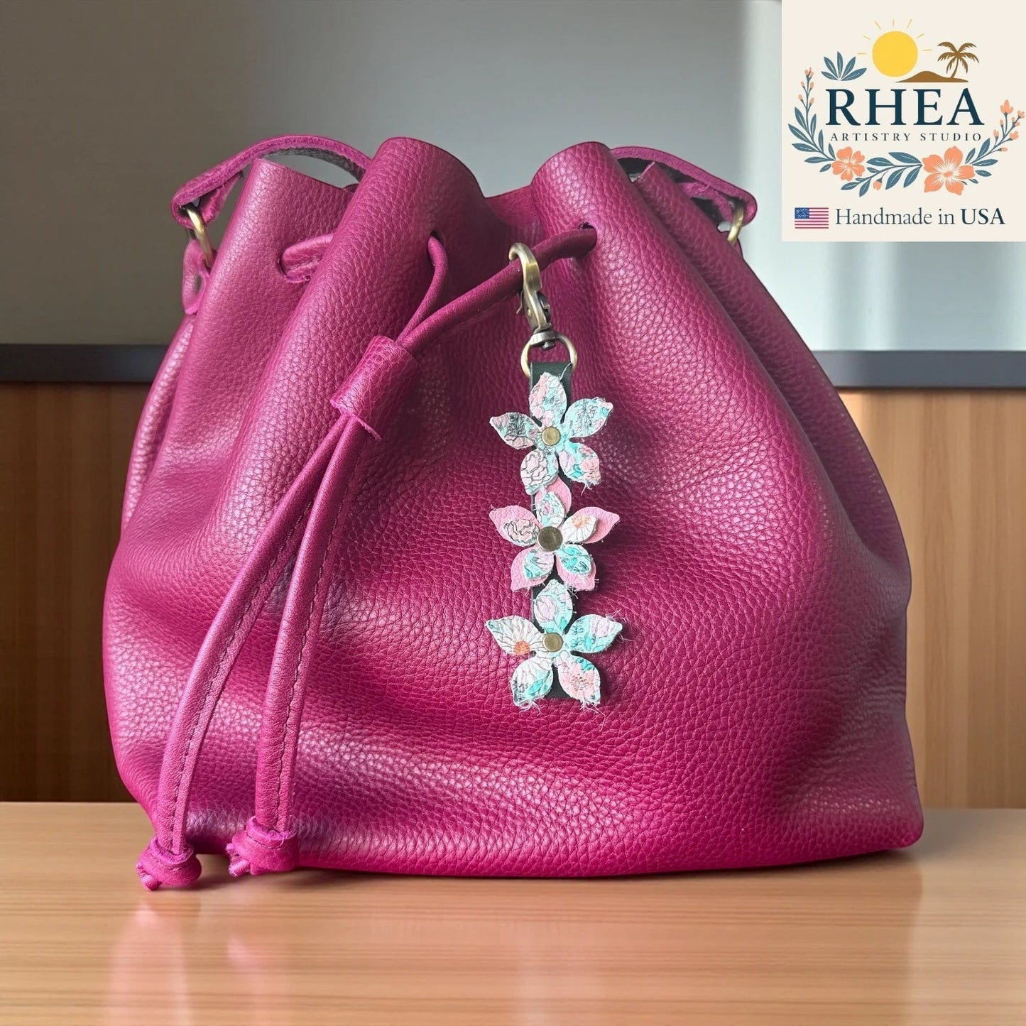 Rhea Artistry Studio handmade leather floral charm with brushed brass clasp on a magenta bucket bag.