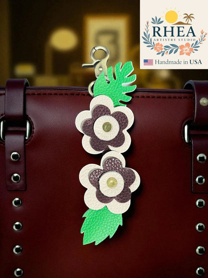 Rhea Artistry Studio handmade leather floral keychain charm with burgundy and cream flowers and green leaves attached to a burgundy bag.