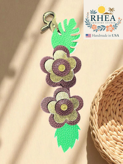 Rhea Artistry Studio handmade leather keychain with burgundy and gold floral charms and green leaves.