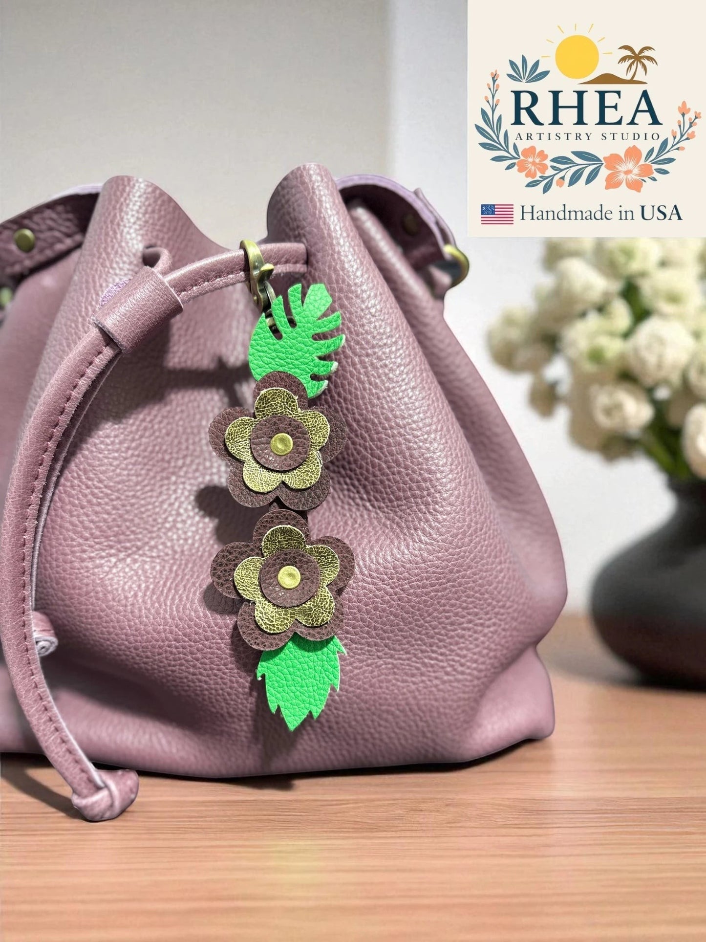 Rhea Artistry Studio handmade leather floral keychain charm with green leaves, attached to a dusty rose bucket bag.