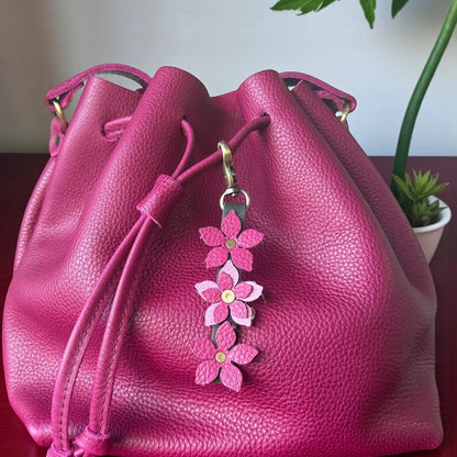 Rhea Artistry Studio handmade leather floral charm with pink flowers and brushed brass clasp attached to a fuchsia drawstring bag.