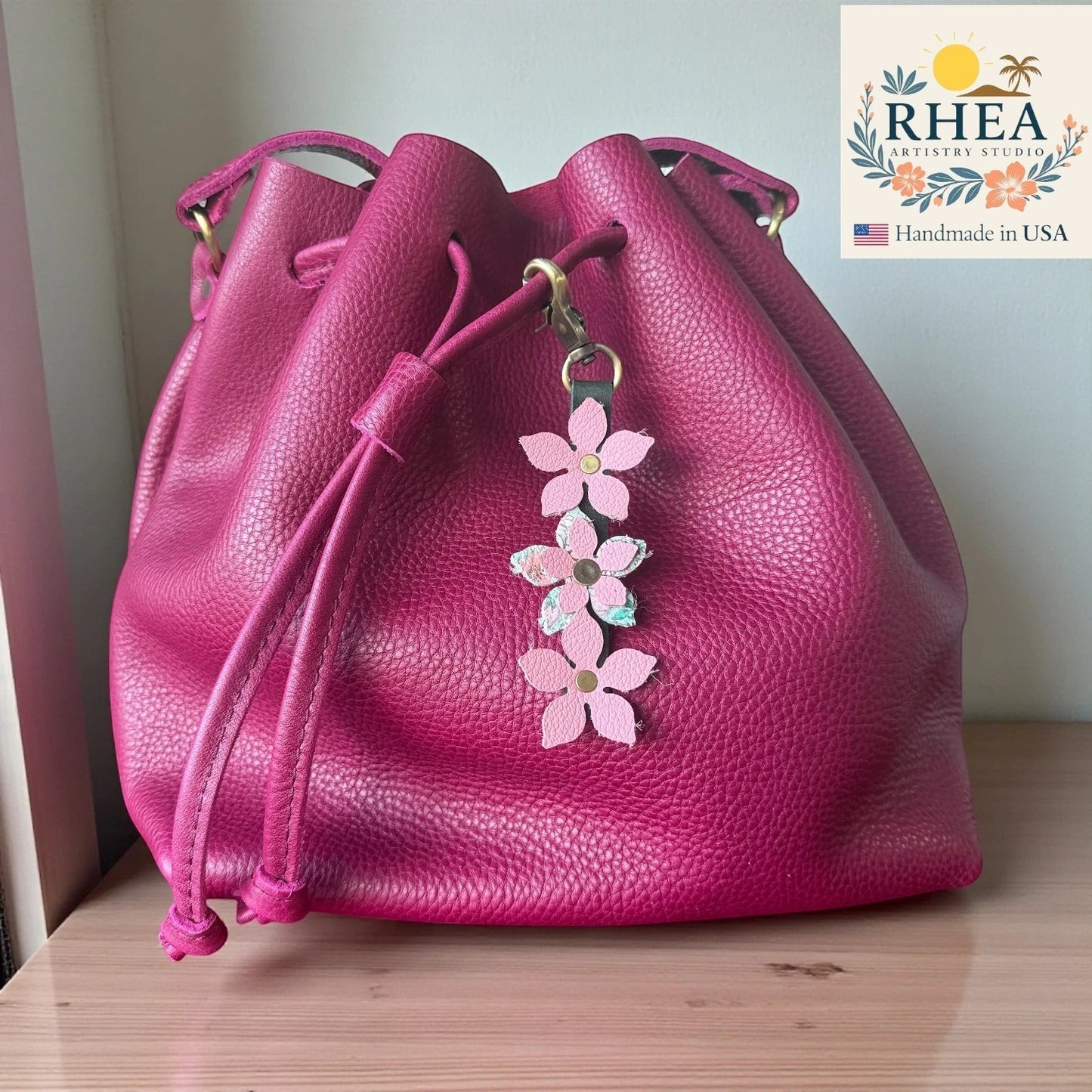 Rhea Artistry Studio handmade leather floral charm with pink flowers and brushed brass clasp on a magenta bucket bag.