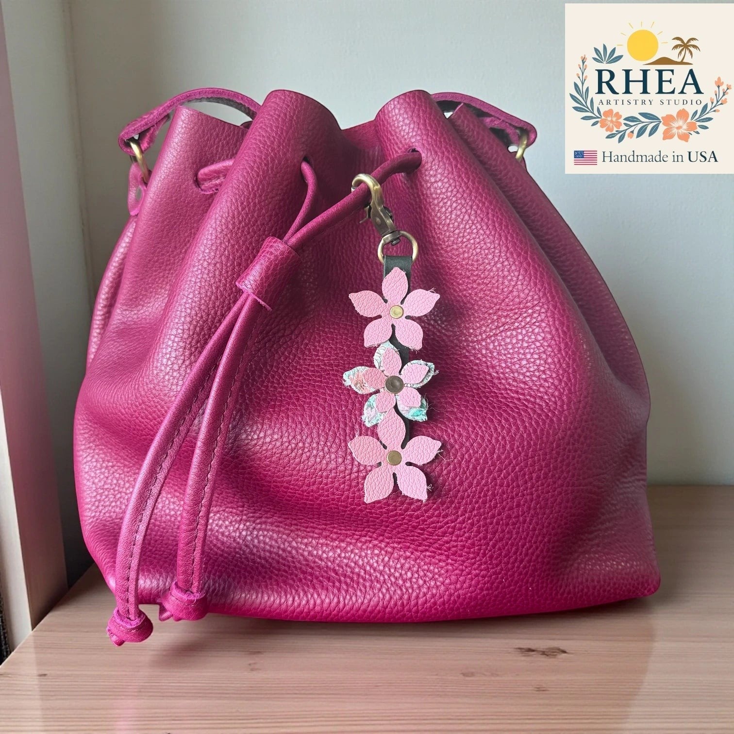 Rhea Artistry Studio handmade leather floral charm with pink flowers and brushed brass clasp on a magenta bucket bag.