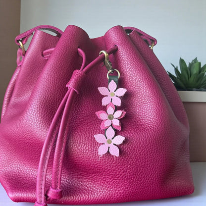Rhea Artistry Studio handmade leather floral charm with pink flowers and brushed brass clasp on a fuchsia bucket bag.