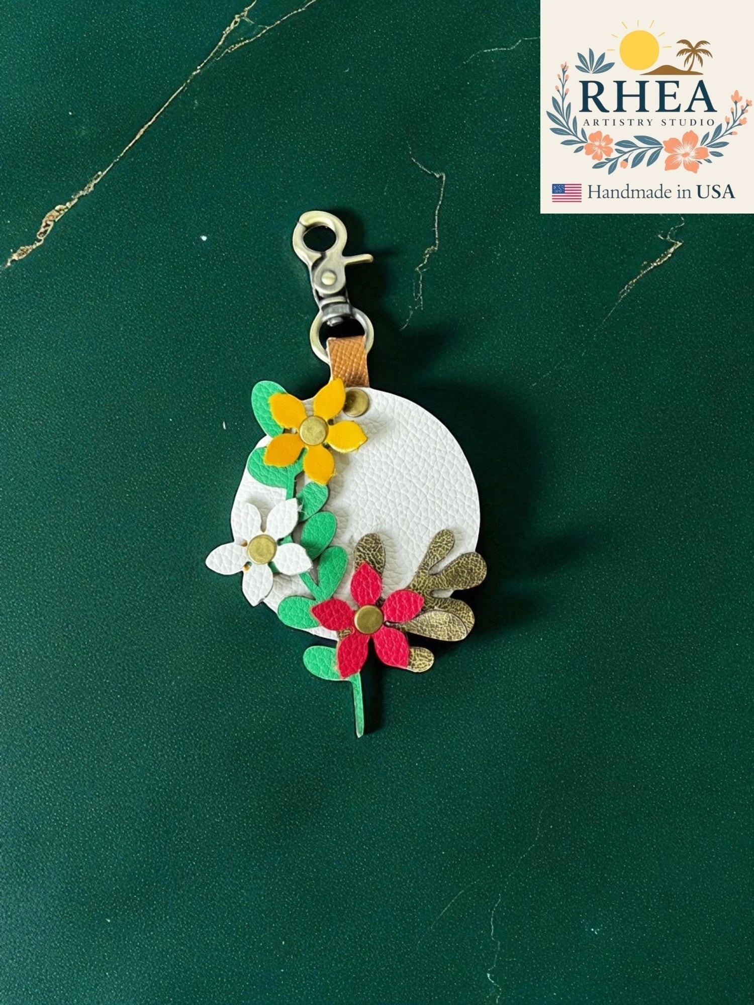 Rhea Artistry Studio white leather charm with layered floral and leaf appliques in red, yellow, green, and gold.