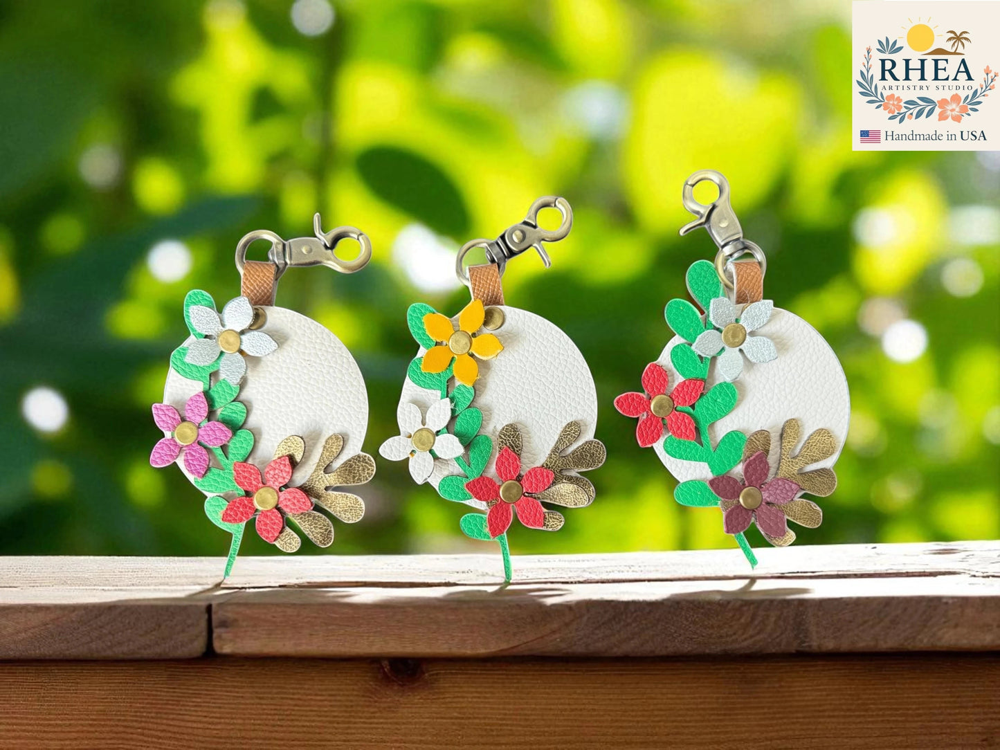 Rhea Artistry Studio white leather circular charm with layered floral and leaf details in pink, red, green, gold, and silver.
