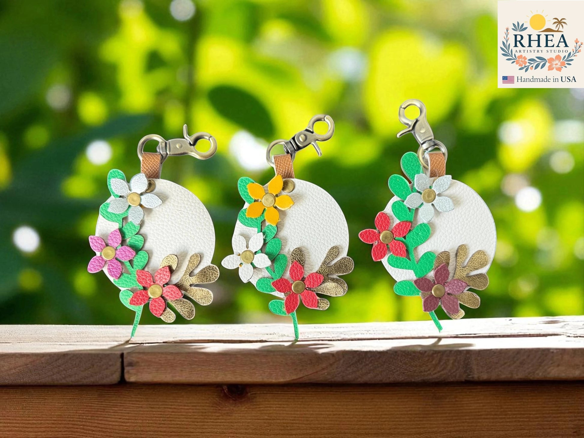 Rhea Artistry Studio white leather circular charm with layered floral and leaf details in pink, red, green, gold, and silver.