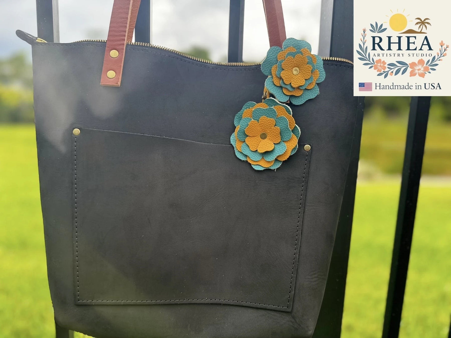 Rhea Artistry Studio handmade double leather flower bag charm in turquoise and yellow, attached to a black tote bag.