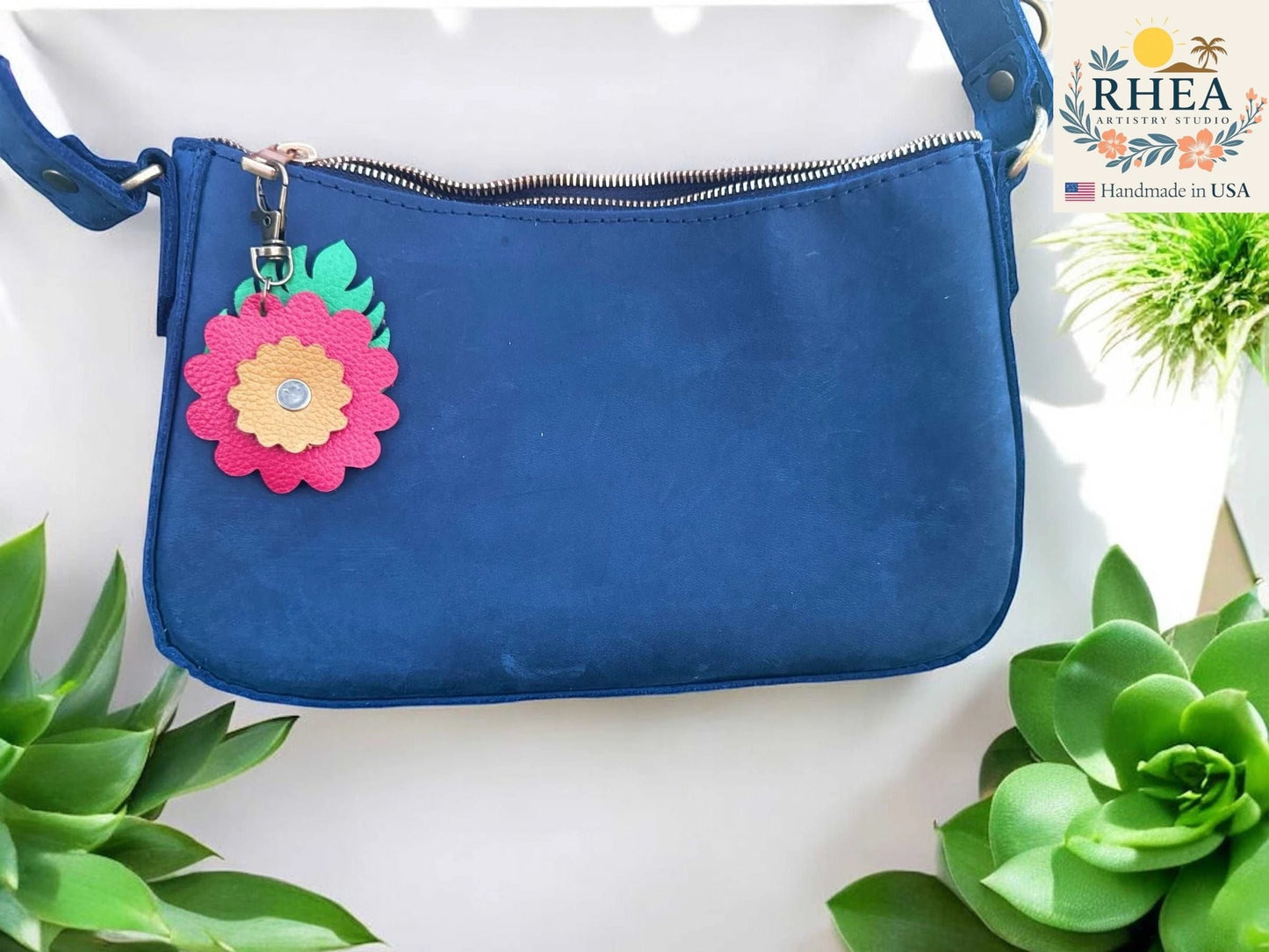 Rhea Artistry Studio leather monstera leaf and flower charm with brass lobster clasp on a blue purse.