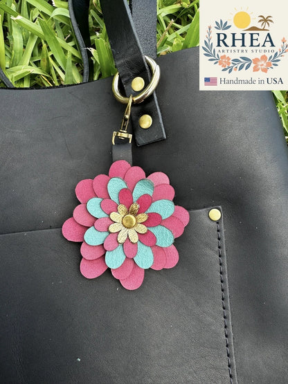 Rhea Artistry Studio multi-color leather flower charm with gold center, attached to a black leather tote bag.