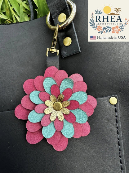 Rhea Artistry Studio multicolored leather flower charm with gold center, attached to a black bag.
