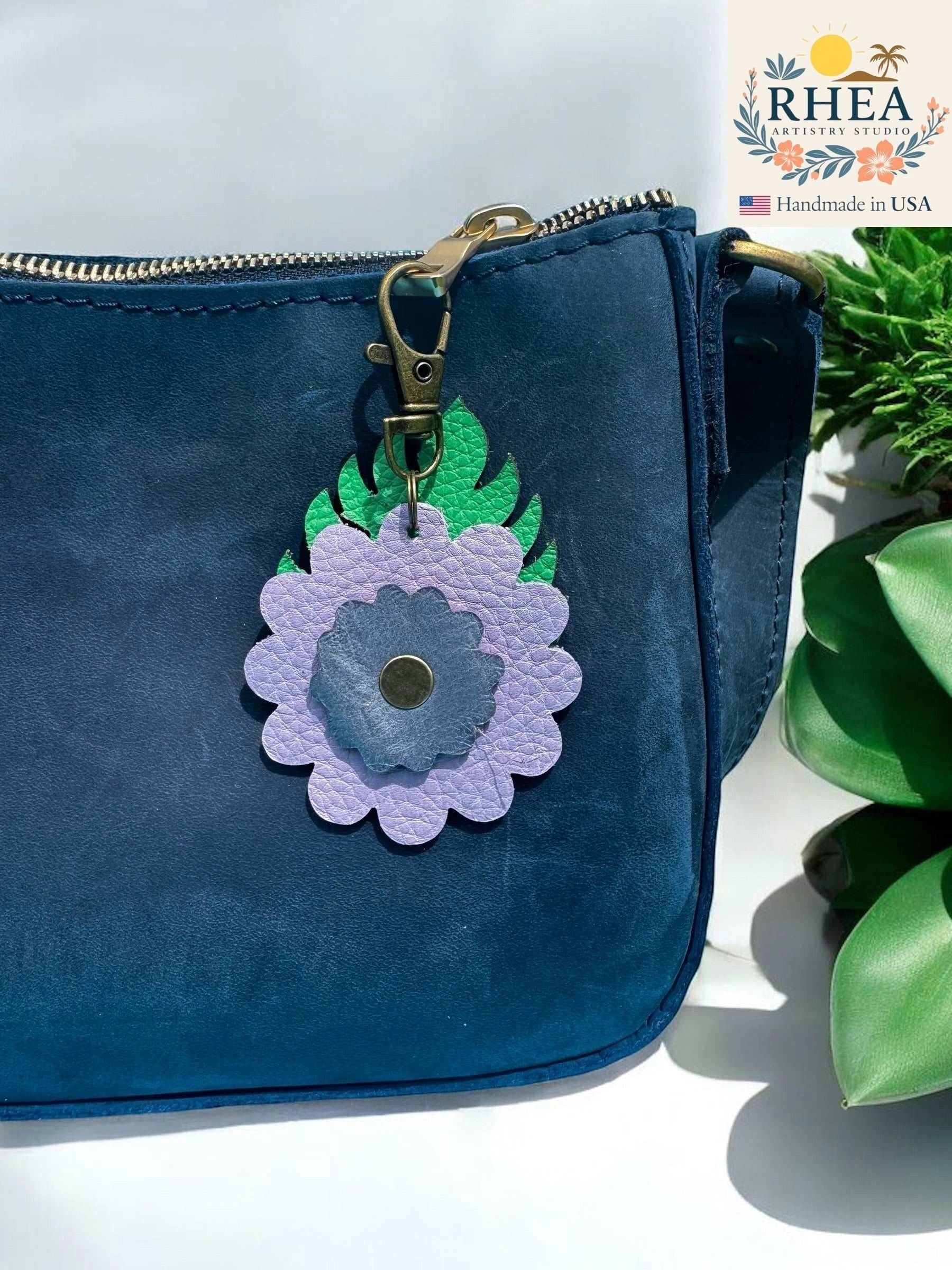 Rhea Artistry Studio leather monstera leaf and flower charm zipper pull in purple and green with brass hardware.