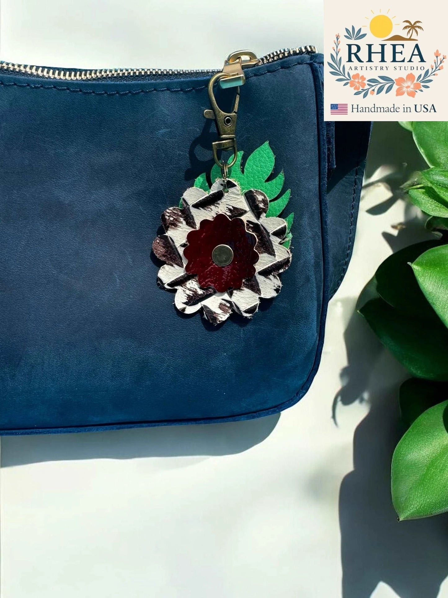 Rhea Artistry Studio leather monstera leaf and flower charm with brass clasp on navy blue purse.