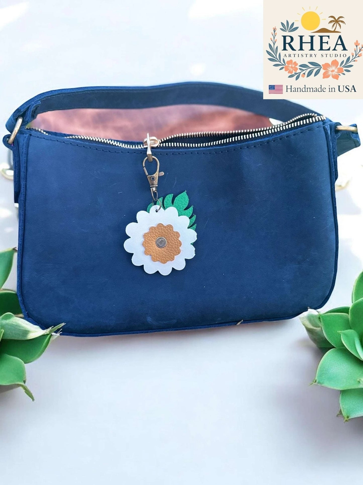 Rhea Artistry Studio leather monstera leaf and flower charm with brass lobster clasp on navy blue purse.