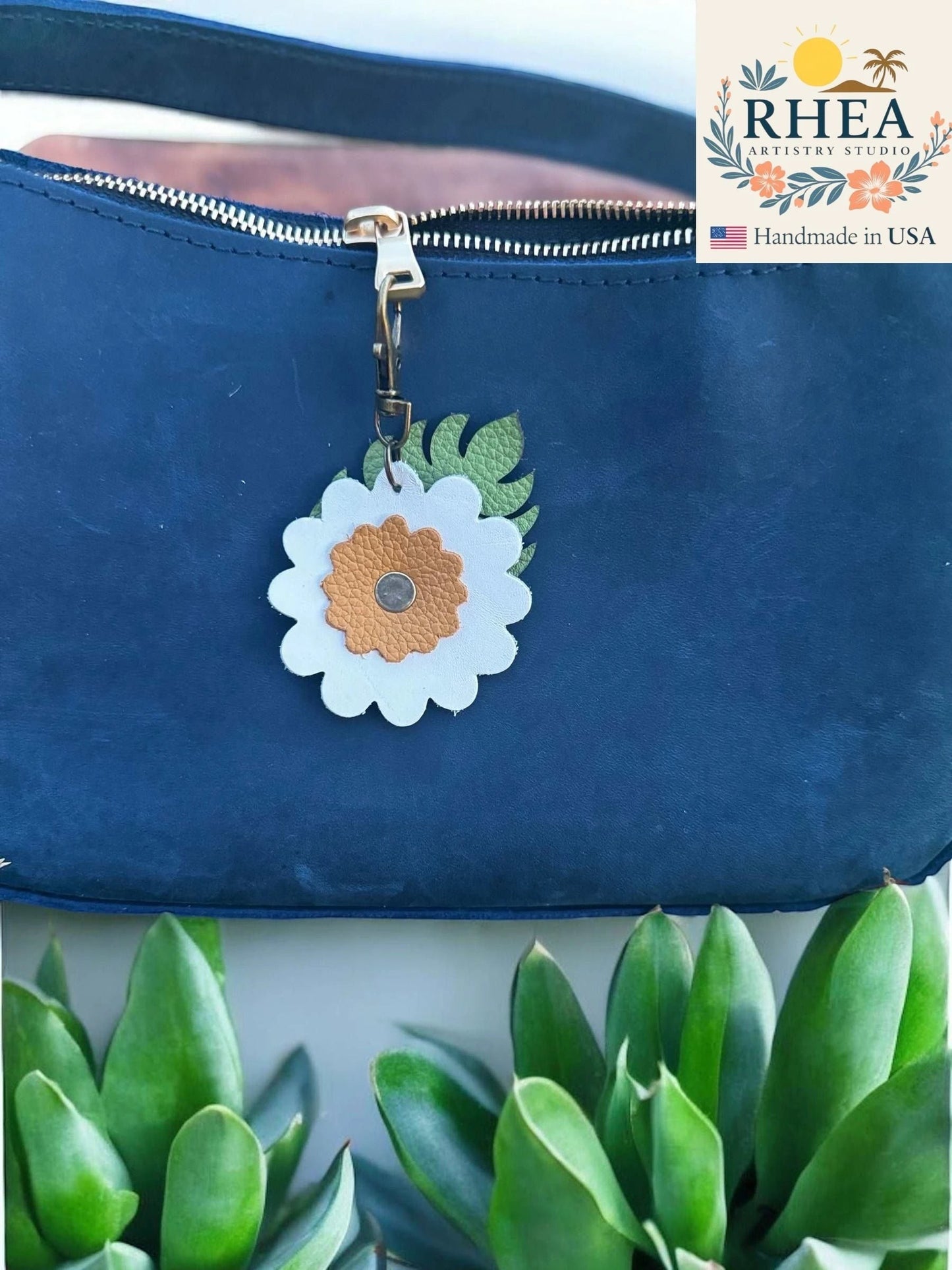 Rhea Artistry Studio leather monstera leaf and flower charm with brass lobster clasp on a navy blue purse.
