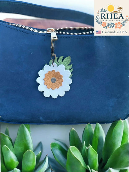 Rhea Artistry Studio leather monstera leaf and flower charm with brass lobster clasp on a navy blue purse.